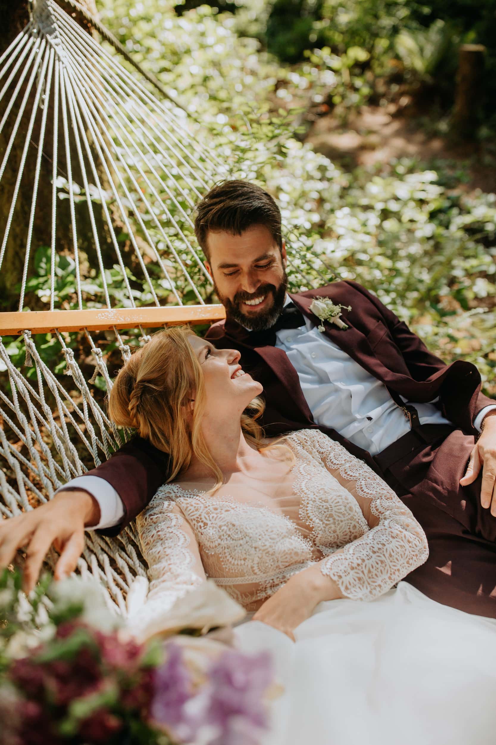 bride and groom looking at each other lying in a hammock