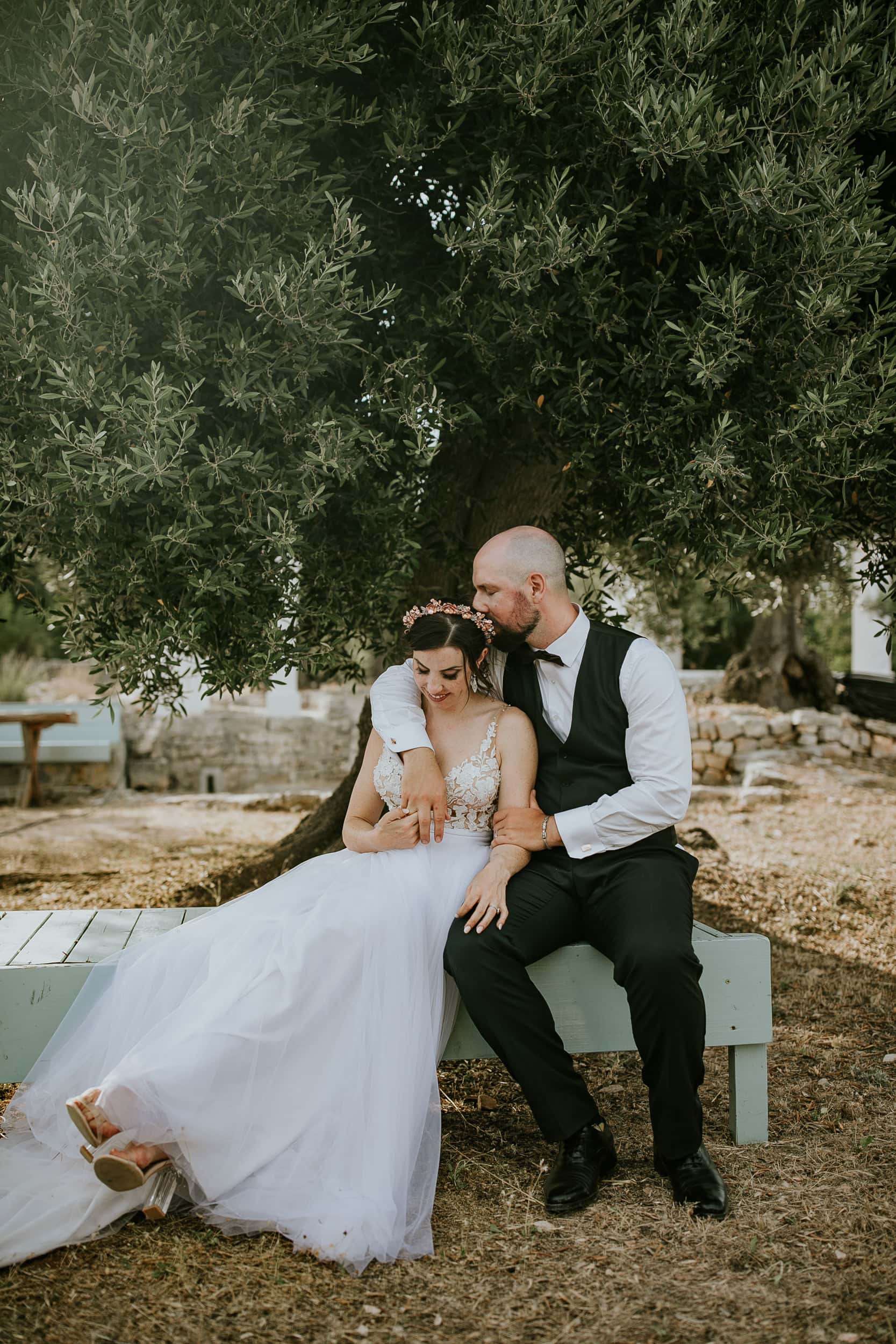 groom kissing bride in front of olive trees